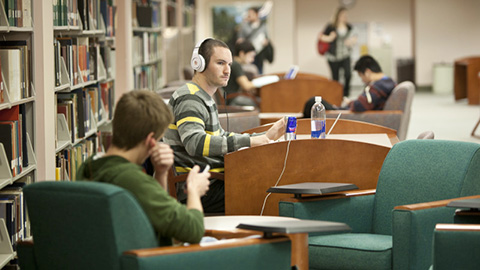 Students working in an open seating area near library stacks.