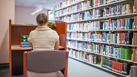 A student sitting at an individual desk near library stacks.