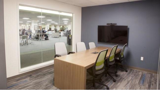 Conference style table and chairs in front of a wall mounted screen.