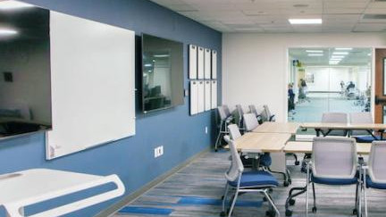 Classroom with two screens, a large whiteboard, and seating.