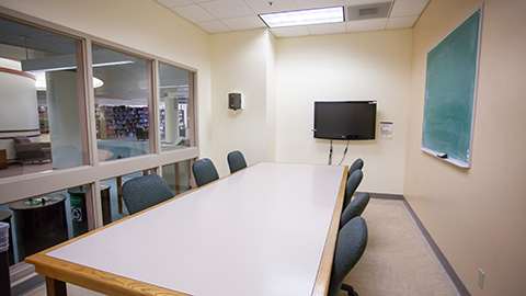 View into group study room with a large table, multiple chairs, a wall mounted screen, and a chalkboard.