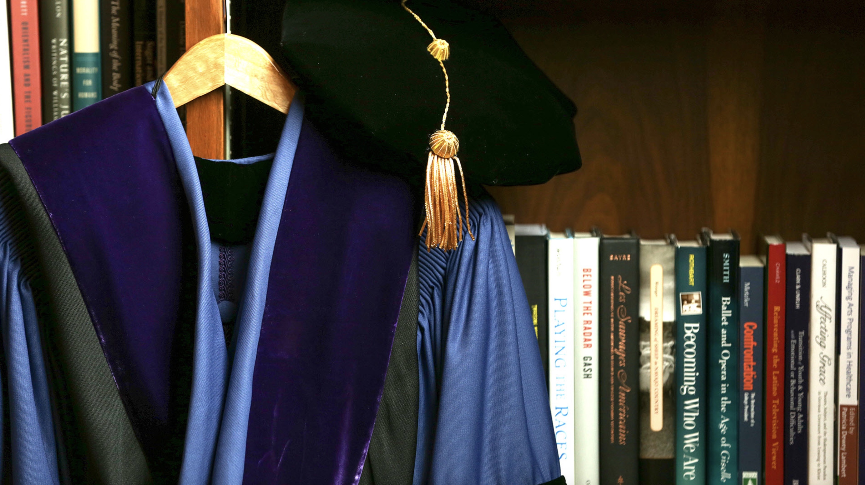 Academic regalia hanging in front of a bookshelf.