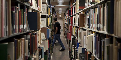 Photograph of a man walking through shelves of books