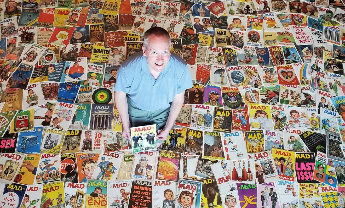 the first 200 issues of MAD magazine spread out on a floor with collector and donor Doug Gilford crouching at the center.