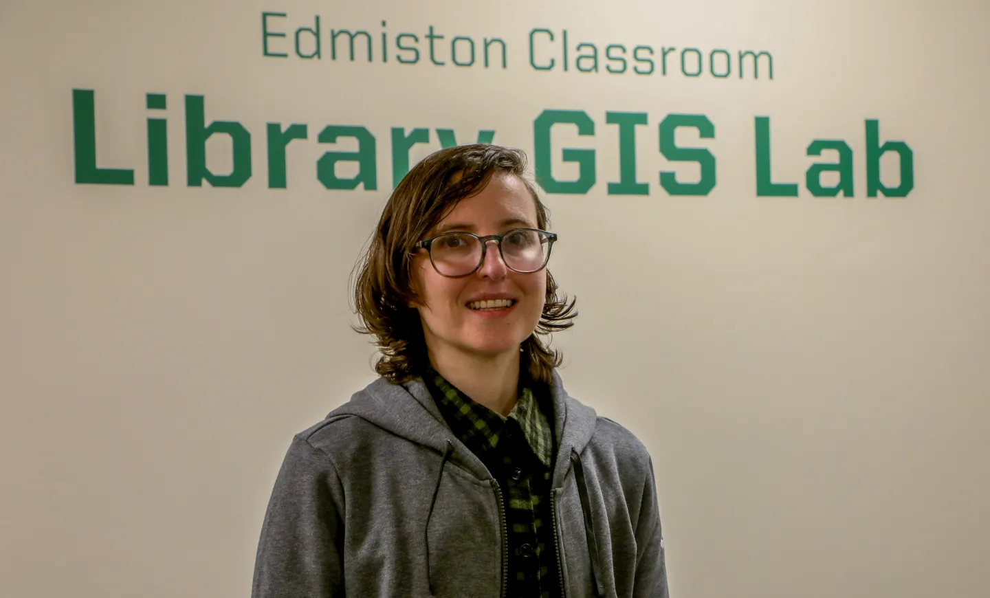 Person is in jean jacket standing in front of signage for the library GIS lab.