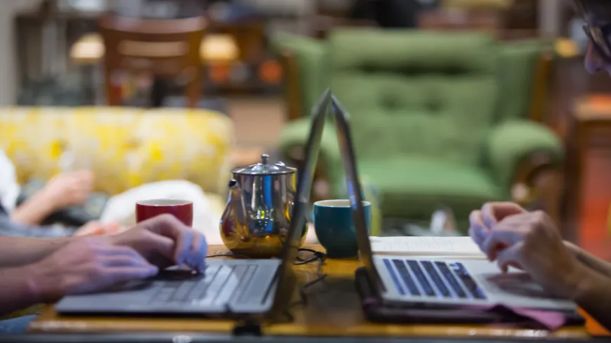 two laptops open with a teapot in the background