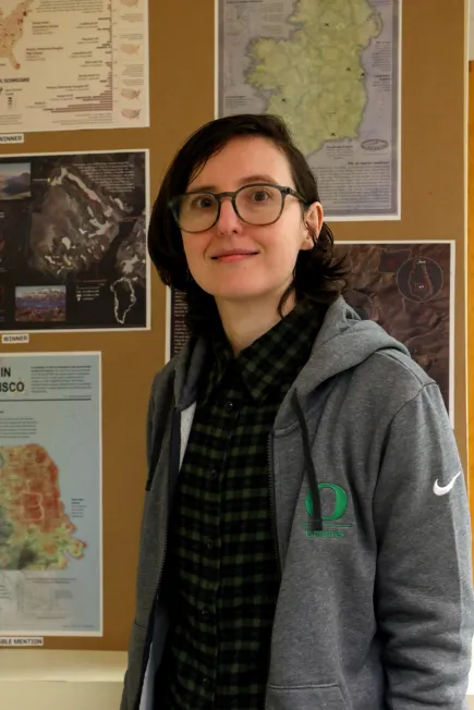 Person wearing gray jacket standing in front of bulletin board with map clippings.