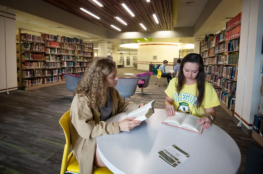 Two students at a table looking at books