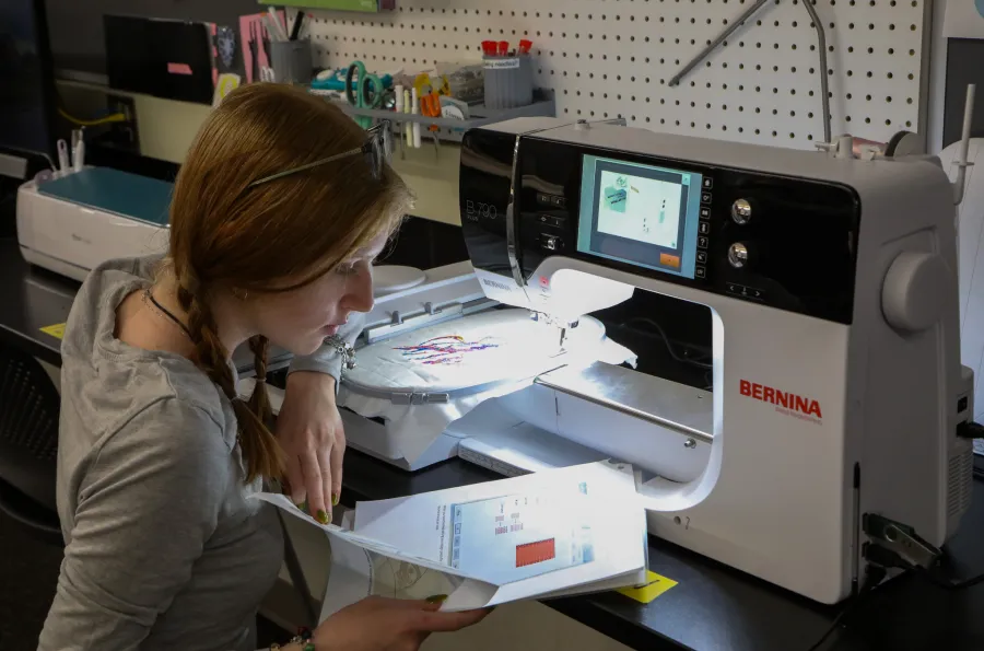 Person sitting at a Bernina embroidery machine and looking over an instruction sheet