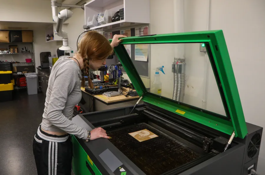 Person holding open the hatch door on a laser cutter and looking at their finished piece